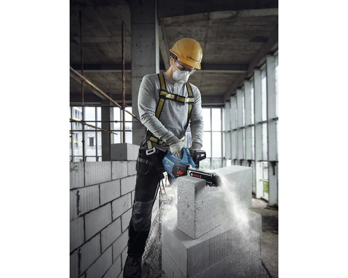 Stavebný robotník reže betónový blok kamennou pílou, používa osobné ochranné prostriedky.