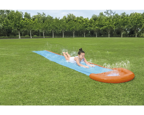 Dievča sa kĺže na vodnej šmýkačke v záhrade