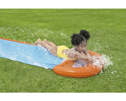 Dievča sa šmýka na vodnej šmýkačke v záhrade.