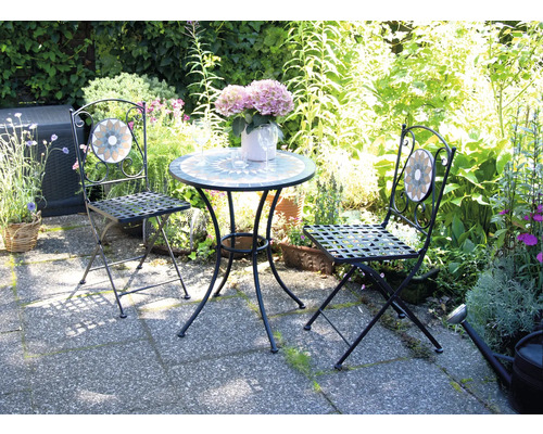 Záhradná scéna so stolom a dvoma stoličkami s mozaikovými detailmi pred bujnou zeleňou