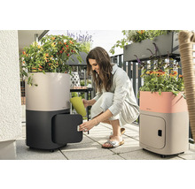 Scéna na balkóne s dvoma kvetináčmi so zavlažovacím systémom, na kolieskach a s úložným priestorom, žena zalieva rastliny