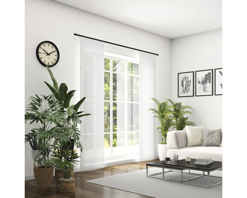 Svetlá obývacia izba s pohovkou, konferenčným stolíkom, izbovými rastlinami, hodinami a posuvným závesom pred oknom.