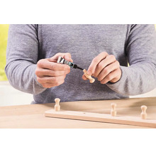 Osoba prilepuje drevený háčik na drevenú lištu lepidlom