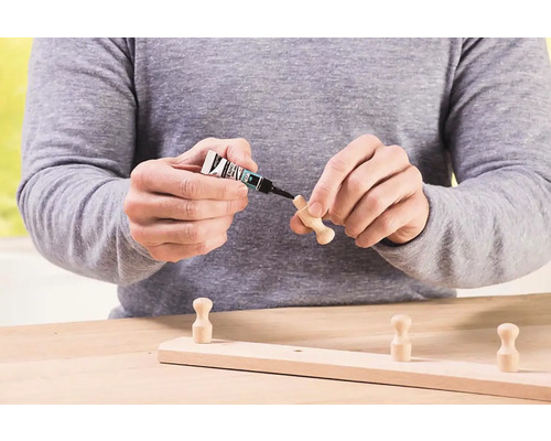 Osoba prilepuje drevený háčik na drevenú lištu lepidlom