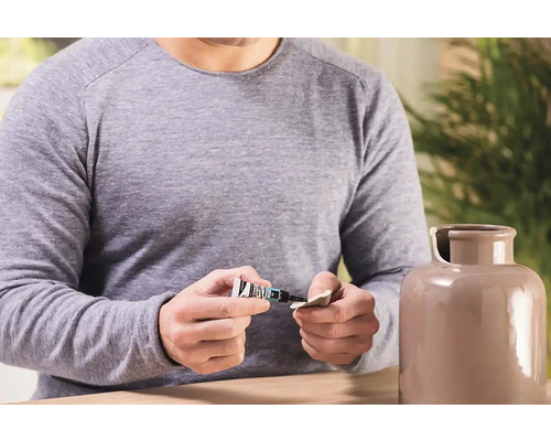 Muž opravuje keramickú vázu lepidlom