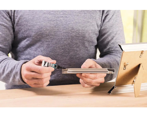 Osoba používa lepidlo na opravu rámu na obraz.