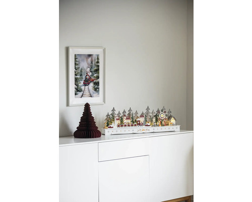 Dekoratívna vianočná scéna s osvetlenou zimnou krajinou, papierovým stromom a obrázkom vlaku na bielej skrini