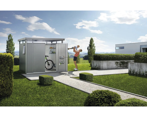 Záhradná scéna s kôlňou na náradie, bicyklom, policami a ženou zdvíhajúcou dieťa