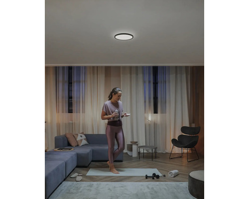 Obývacia izba so stropným svietidlom, pohovkou a cvičiacou ženou