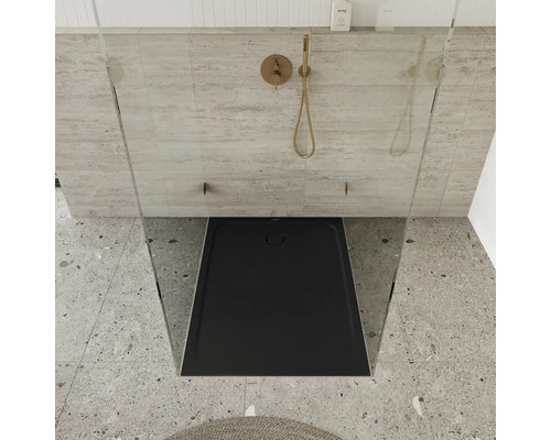 Sprchovací kút v úrovni podlahy s čiernou sprchovacou vaničkou a pozlátenou armatúrou.