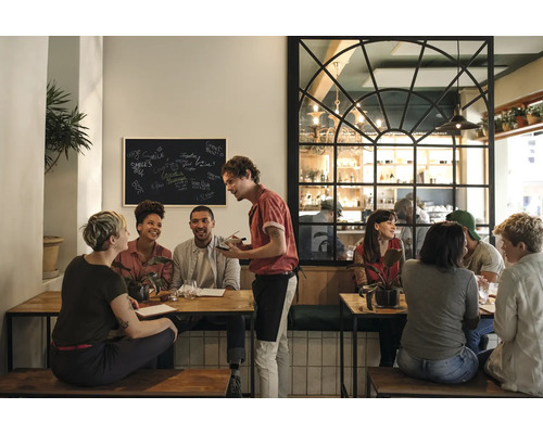 Scéna v reštaurácii s hosťami pri stoloch a čašníkom, ktorý prijíma objednávky.