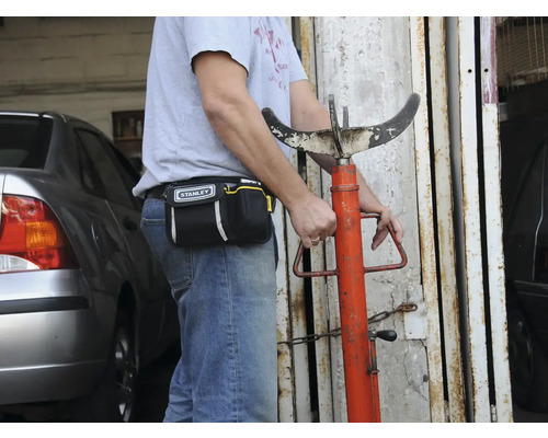 Osoba s brašňou na náradie značky Stanley a podperou prevodovky.