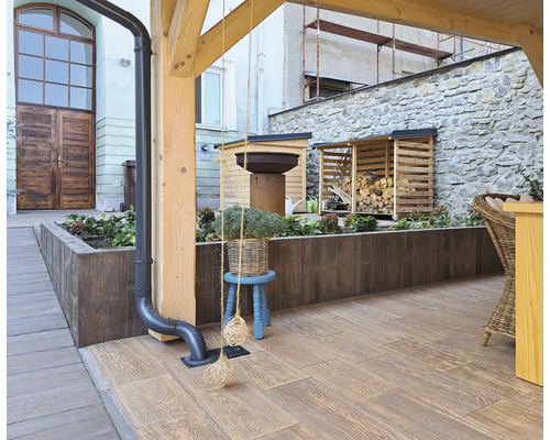 Exteriér s terasovou dlažbou vo vzhľade dreva, skladom dreva a kvetináčmi na rastliny