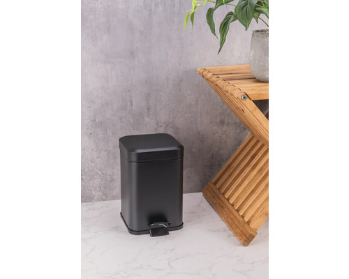 Čierny kovový odpadkový kôš vedľa drevenej stoličky s rastlinou