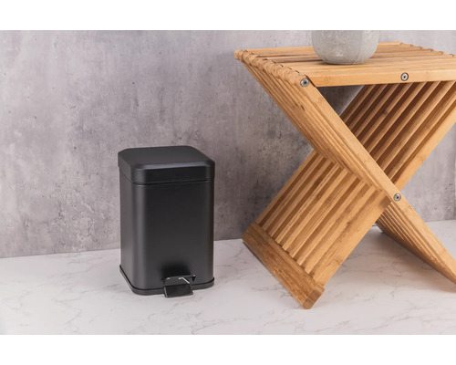 Čierny kovový odpadkový kôš vedľa drevenej stoličky.