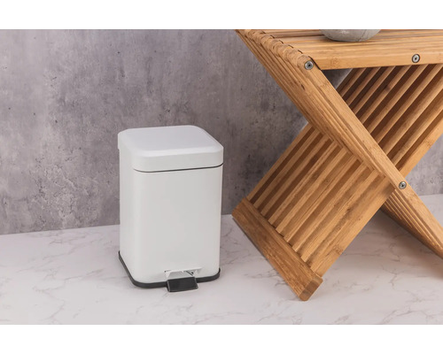 Biely kovový pedálový kôš vedľa drevenej stoličky