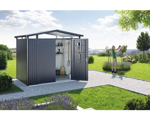 Záhradná scéna s kôlňou na náradie, záhradným náradím a ženou pracujúcou v záhrade.