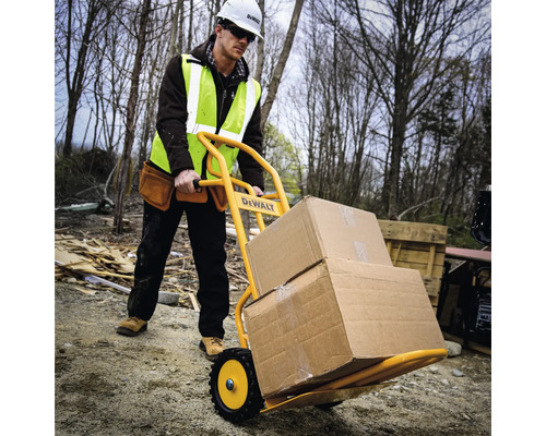 Stavebný robotník prepravuje kartóny rudlom na stavenisku. Rudel je žltý a má logo DeWalt.