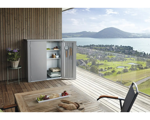 Kovová záhradná skrinka s otvorenými dverami na terase s výhľadom na jazero a hory