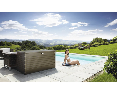 Scéna s kovovým úložným boxom vedľa bazéna, obklopeného záhradným nábytkom a ženou sediacou vo vode.