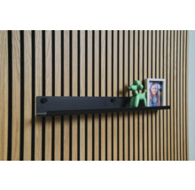 Čierna nástenná polica pred drevenou obkladovou stenou s dekoráciou