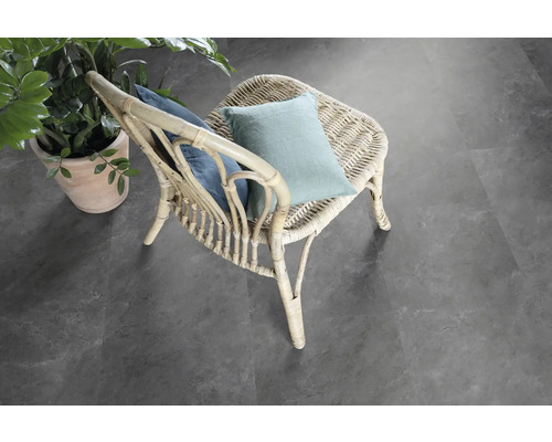 Scéna s ratanovým kreslom s vankúšmi a črepníkovou rastlinou na šedej podlahe.