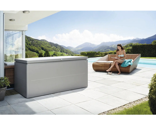 Záhradný box na podušky Biohort LoungeBox 200, 200x84x88,5 cm sivý metalický Vonkajšia scéna s veľkým úložným boxom vedľa sediacej ženy na pohovke pri bazéne s výhľadom na horskú krajinu