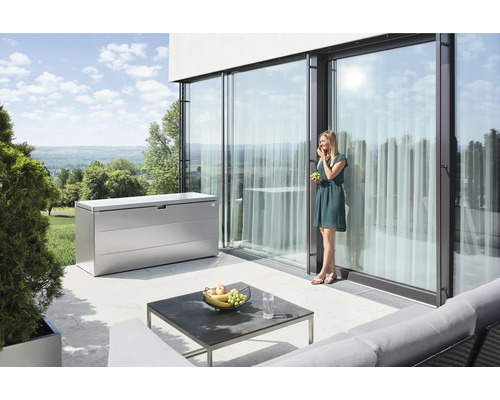 Scéna s kovovým úložným boxom na terase, stolom a ženou, ktorá je hrozno