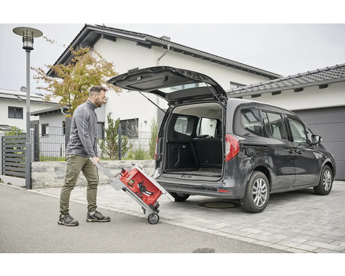 Muž nakladá stolovú pílu s prepravným vozíkom do auta.