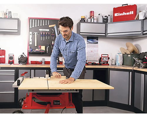 Muž pracuje so stolovou pílou v dielni s náradím a skrinkami.