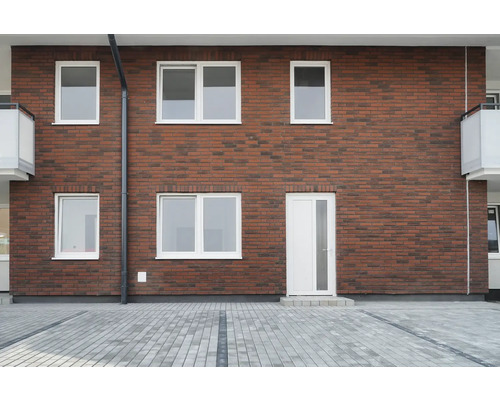 Fasáda domu s tehlovou stenou, bielymi oknami a dverami