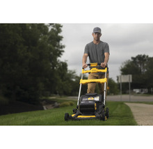 Muž obsluhuje žltú kosačku na trávu značky DeWalt v záhrade.