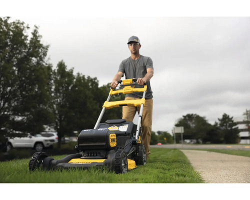 Muž tlačí žlto-čiernu kosačku na trávu v záhrade.