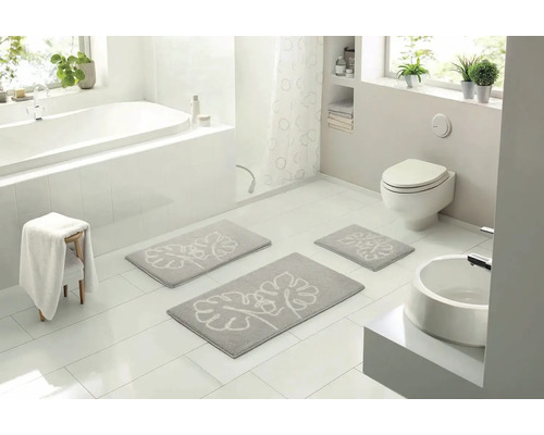 Svetlá kúpeľňa s vaňou, toaletou a umývadlom a sivou súpravou kúpeľňových predložiek s rastlinným vzorom.