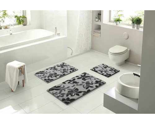 Svetlá kúpeľňa s vaňou, umývadlom a tromi sivými kúpeľňovými predložkami s kvetinovým vzorom