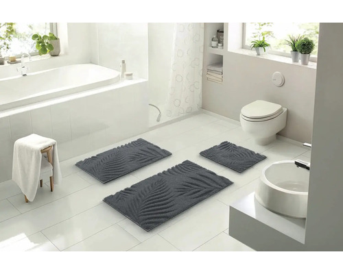 Svetlá kúpeľňa s vaňou, toaletou a umývadlom a súprava kúpeľňových koberčekov s motívom listov.