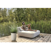 Muž relaxuje na záhradnom lehátku so slúchadlami, vedľa neho kvetináč s okrasnou trávou na drevenej terase.