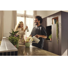 Muž a žena sa starajú o izbové rastliny s kanvou a rozprašovačom vo svetlej miestnosti.