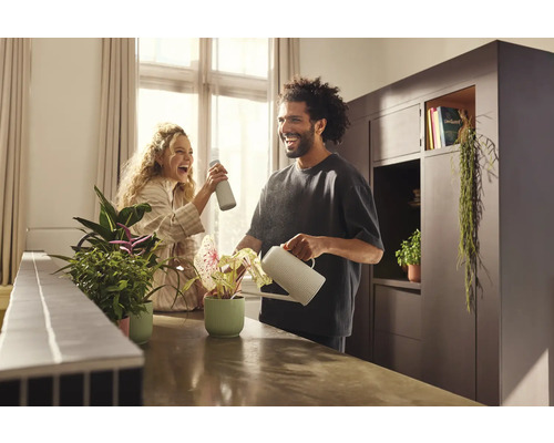 Muž polieva izbovú rastlinu kanvou, zatiaľ čo žena používa rozprašovač na rastliny