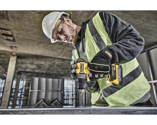 Stavebný robotník vŕta žltou vŕtačkou otvor do kusu kovu.