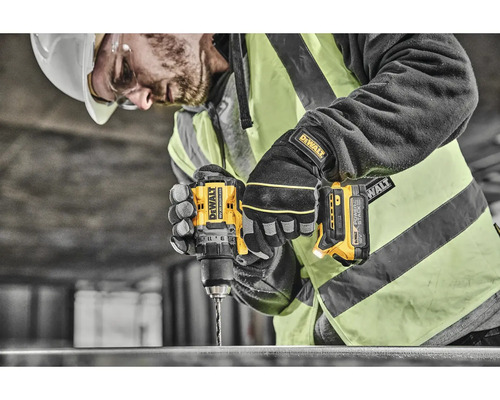 Stavebný robotník s ochrannou helmou a okuliarmi vŕta žltým akumulátorovým vŕtacím skrutkovačom DeWalt do obrobku