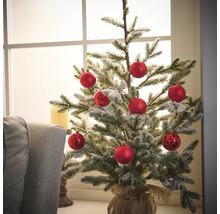 Zdobený malý vianočný stromček s červenými guľami v jutovom vreci