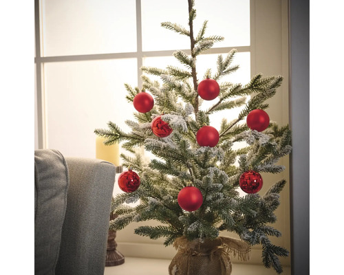 Zdobený malý vianočný stromček s červenými guľami v jutovom vreci