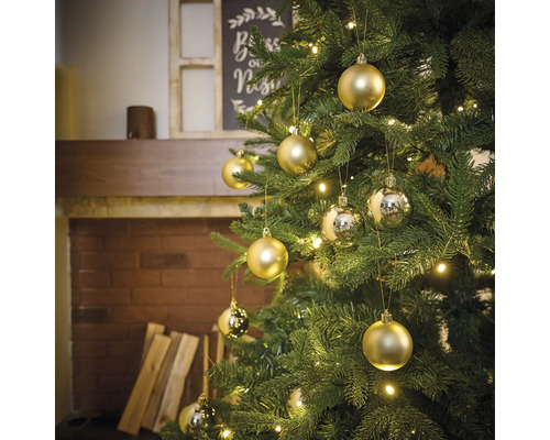 Ozdobený vianočný stromček so zlatými a striebornými ozdobami a svetlami v obývacej izbe s krbom