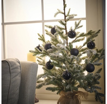 Dekoratívny zasnežený vianočný stromček s čiernymi guľami na stole pri okne