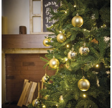 Ozdobený vianočný stromček so zlatými guľami a svetlami v miestnosti s krbom.