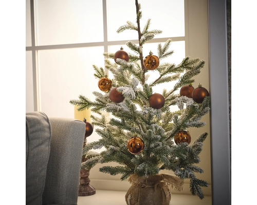 Zdobený zasnežený vianočný stromček s hnedými ozdobami v jutovom vreci