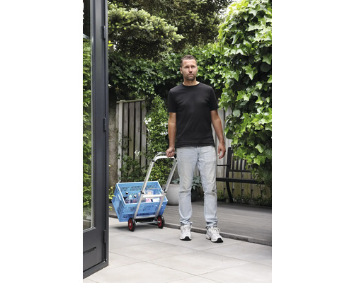 Muž prepravuje modrý nákupný box s vozíkom v záhrade