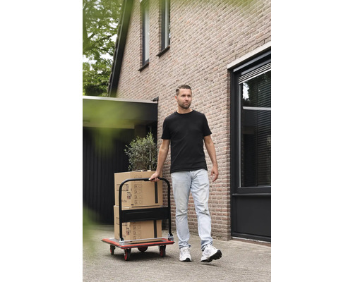 Muž prepravuje sťahovacie krabice s prepravným vozíkom pred domom.