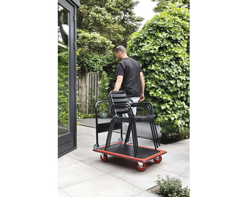 Osoba prepravuje stoličky v záhrade pomocou skateboardu.